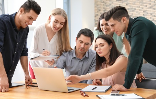 6 Einkaufsfachfrauen und Einkaufsfachmänner schauen zusammen auf einen Laptop und diskutieren